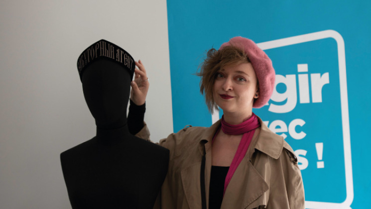 Daria Serenko se tenant aux côtés de la coiffe russe acquise par le Musée départemental de la Résistance & de la Déportation